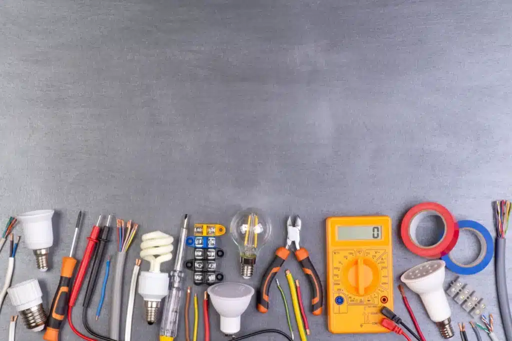 Matériel d'électricien disposé sur une table, comprenant des ampoules, un multimètre et divers outils pour l'installation électrique.